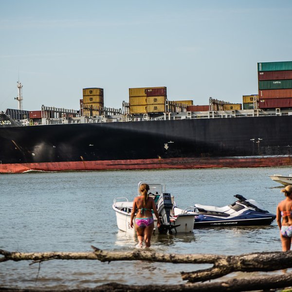 group of people wading near large ships transporting shipping containers
